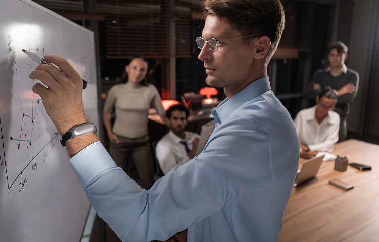 Mann trägt einen silbernen Plaud NotePin am Handgelenk und zeichnet ein Diagramm auf ein Whiteboard.
