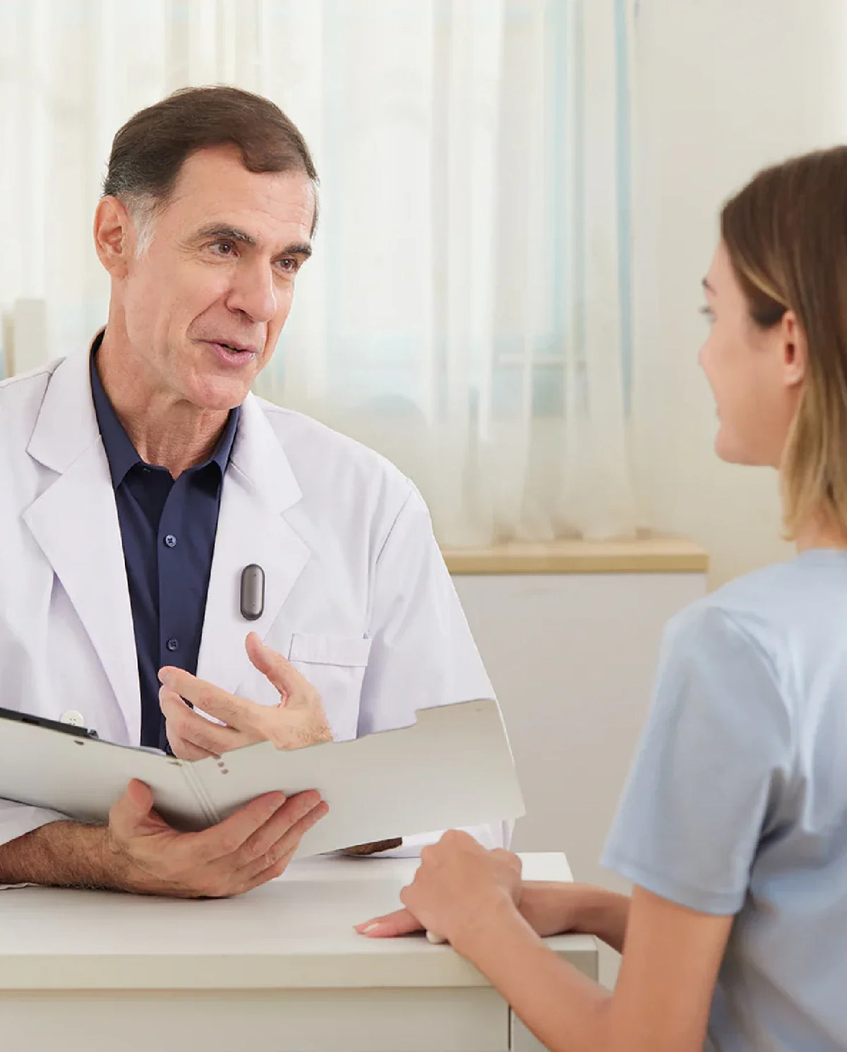 Ein Arzt trägt einen Plaud NotePin am Kittel während eines Beratungsgesprächs mit einer Patientin.