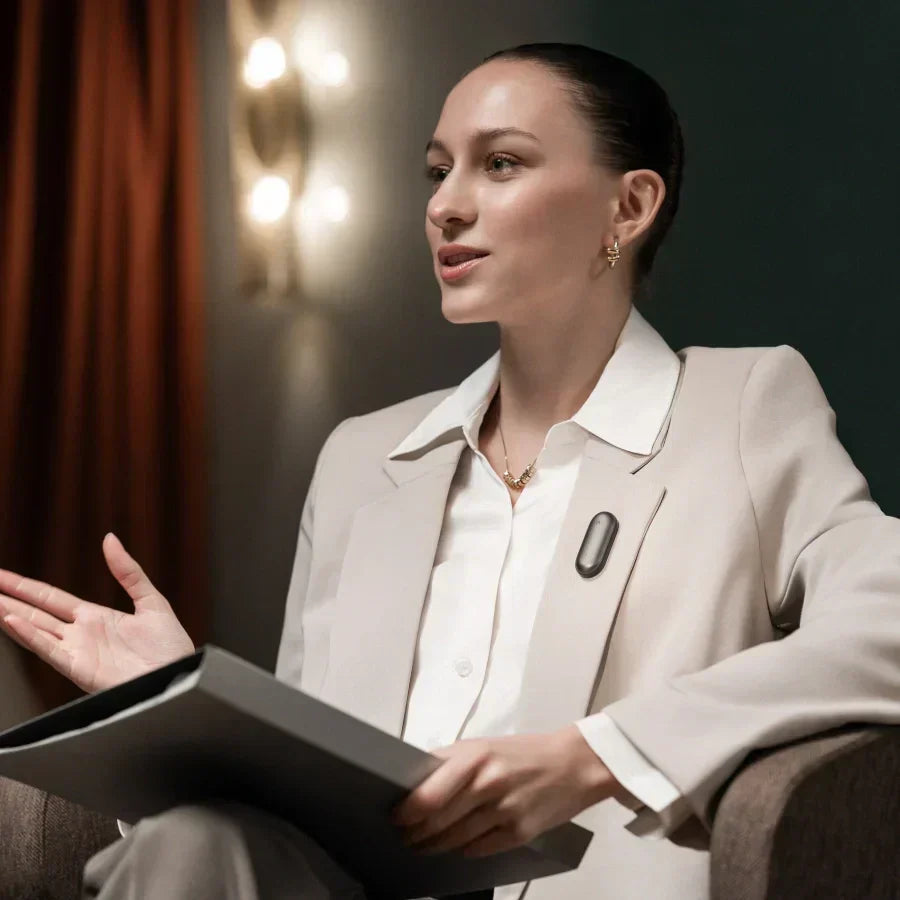 Frau im beigen Blazer trägt den schwarzen Plaud NotePin am Revers während eines professionellen Gesprächs.