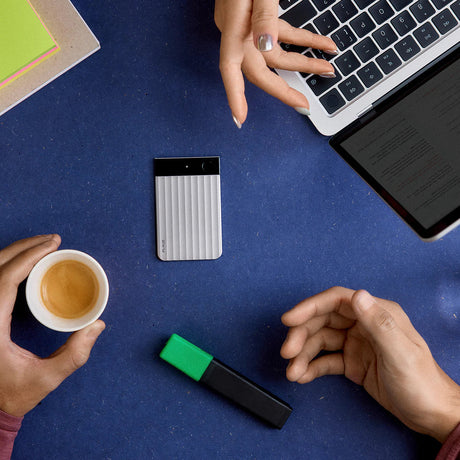 Graues Handheld-Gerät, Kaffee, Laptop und Marker auf blauem Tisch