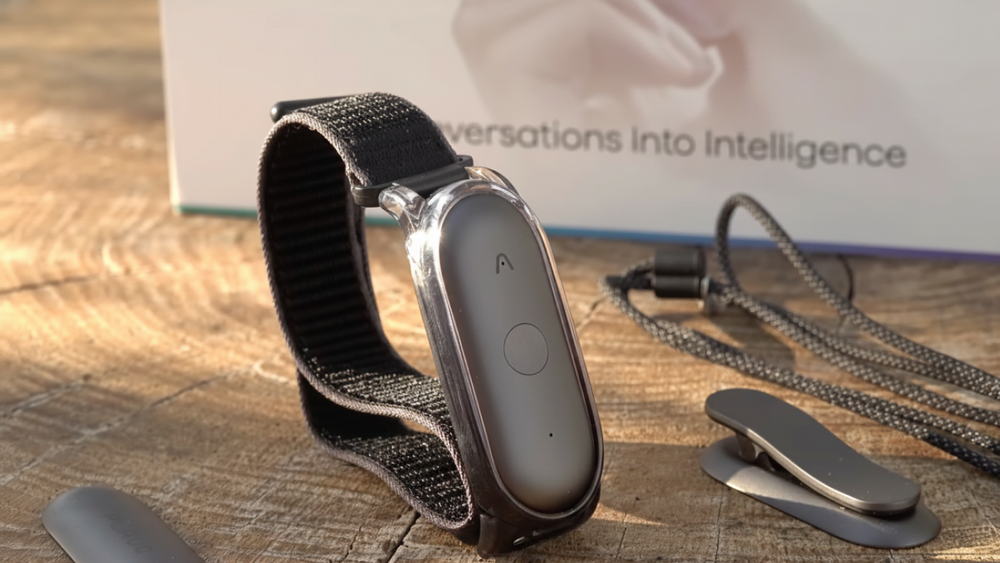 Plaud NotePin in Cosmic Gray mit schwarzem Armband, Clip und Lanyard auf einer Holzoberfläche.