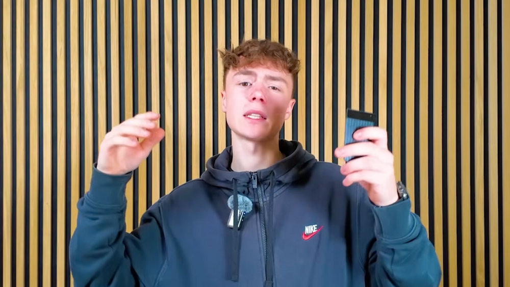 Junger Mann präsentiert den schwarzen Plaud Note Pro AI-Diktiergerät vor einer Wand mit Holzlamellen.