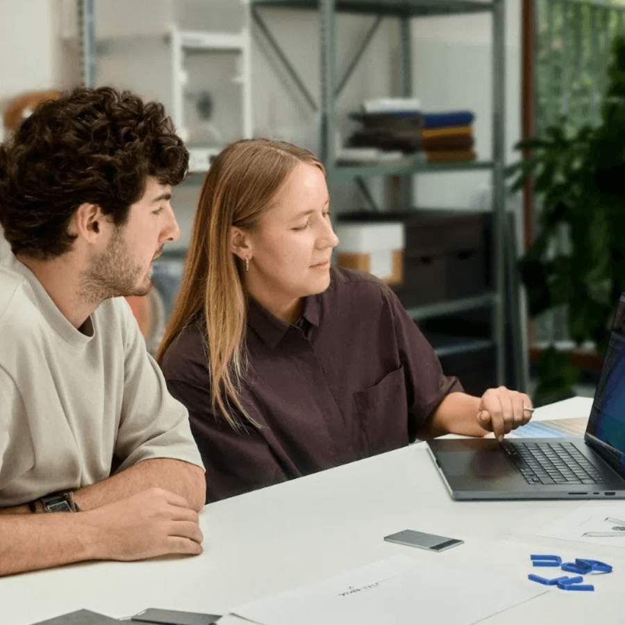Zwei Kollegen besprechen Projekte am Laptop; ein silberner Plaud Note Pro liegt griffbereit auf dem Tisch.