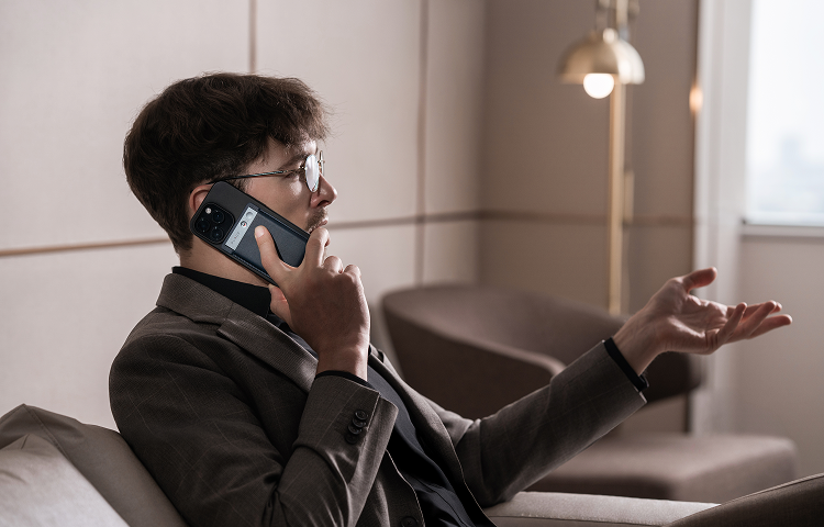 Ein Mann telefoniert mit einem Smartphone, auf dem ein schwarzer Plaud Note zur KI-Aufzeichnung befestigt ist.