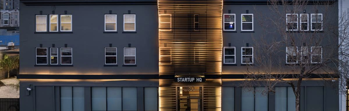 Fassade eines modernen Bürogebäudes mit dem Schild 'STARTUP HQ' bei Nacht.