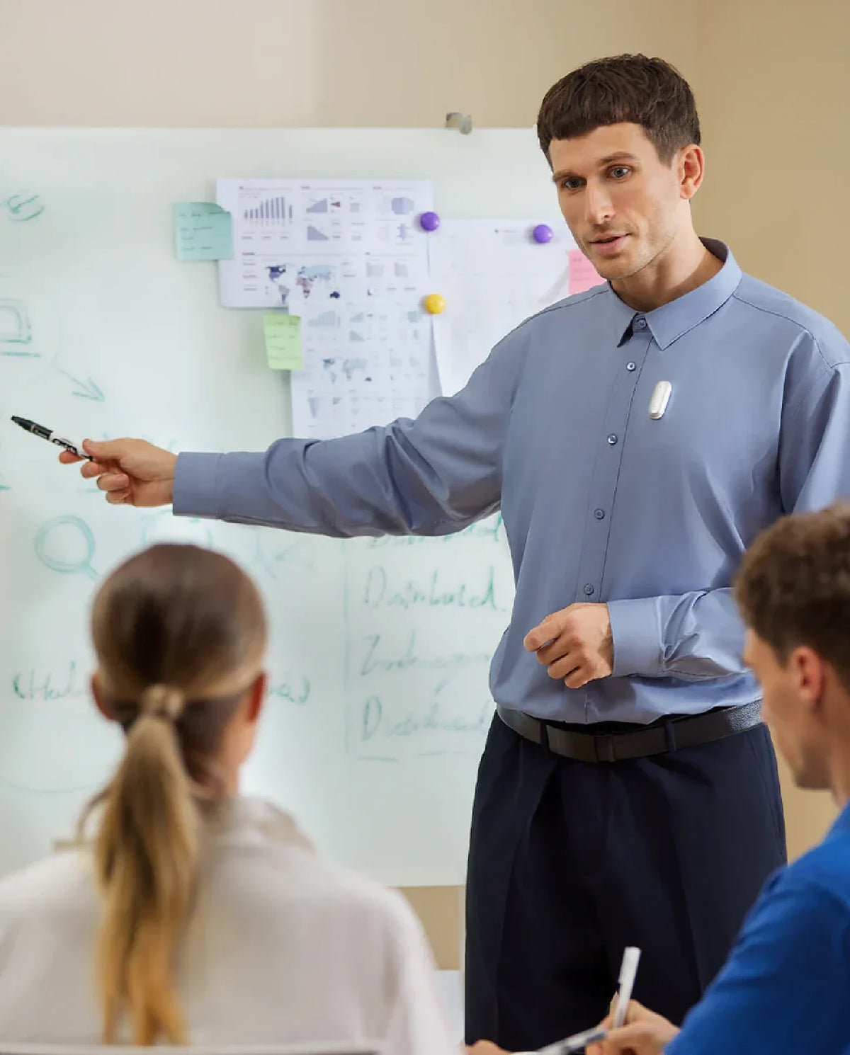 Ein Mann trägt einen silbernen Plaud NotePin am Hemd während einer Präsentation vor einem Whiteboard.