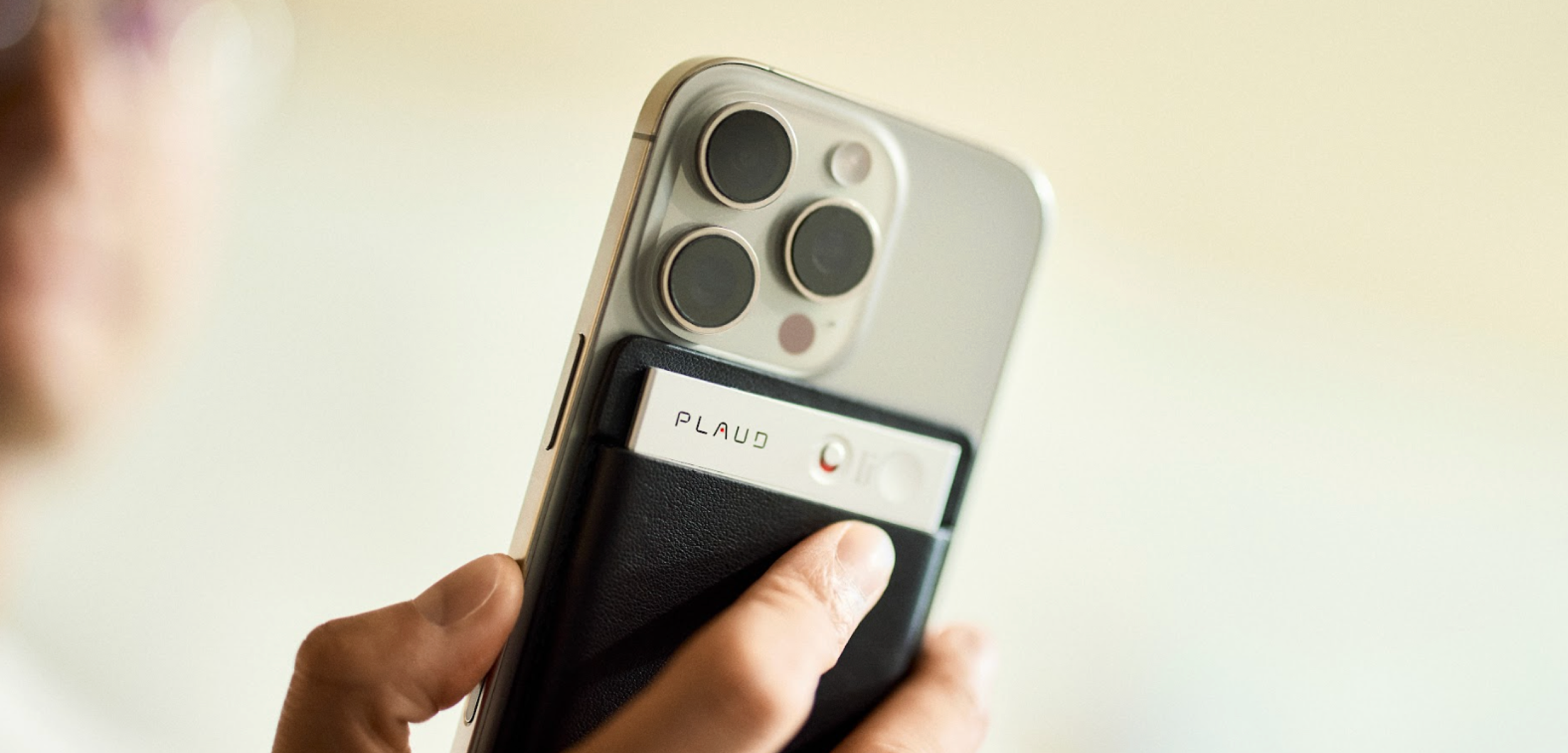 Ein silberner Plaud Note an einem Smartphone, während ein Finger die Aufnahmetaste betätigt.