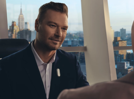 Geschäftsmann trägt ein silbernes Plaud NotePin am Revers in einem Büro mit Blick auf die Skyline von New York.